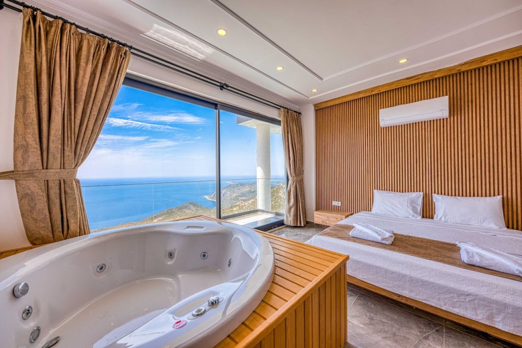 Modern hotel bedroom with in-room Jacuzzi tub, ocean view windows, wooden accents, and minimalist design